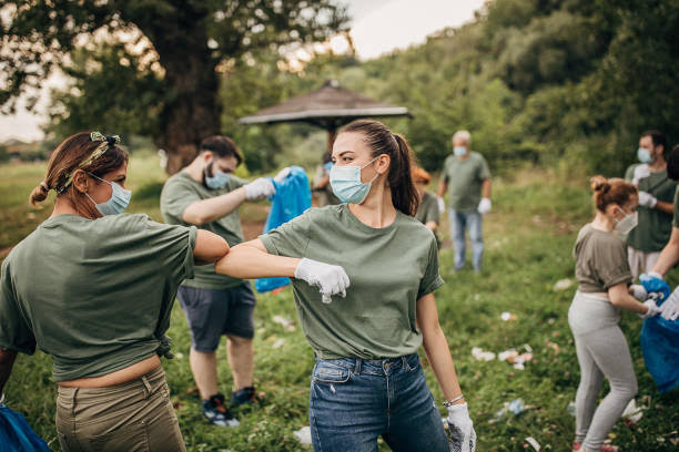 Several people standing in a field. They are all wearing masks for safety. Two are bumping their elbows together in joy.