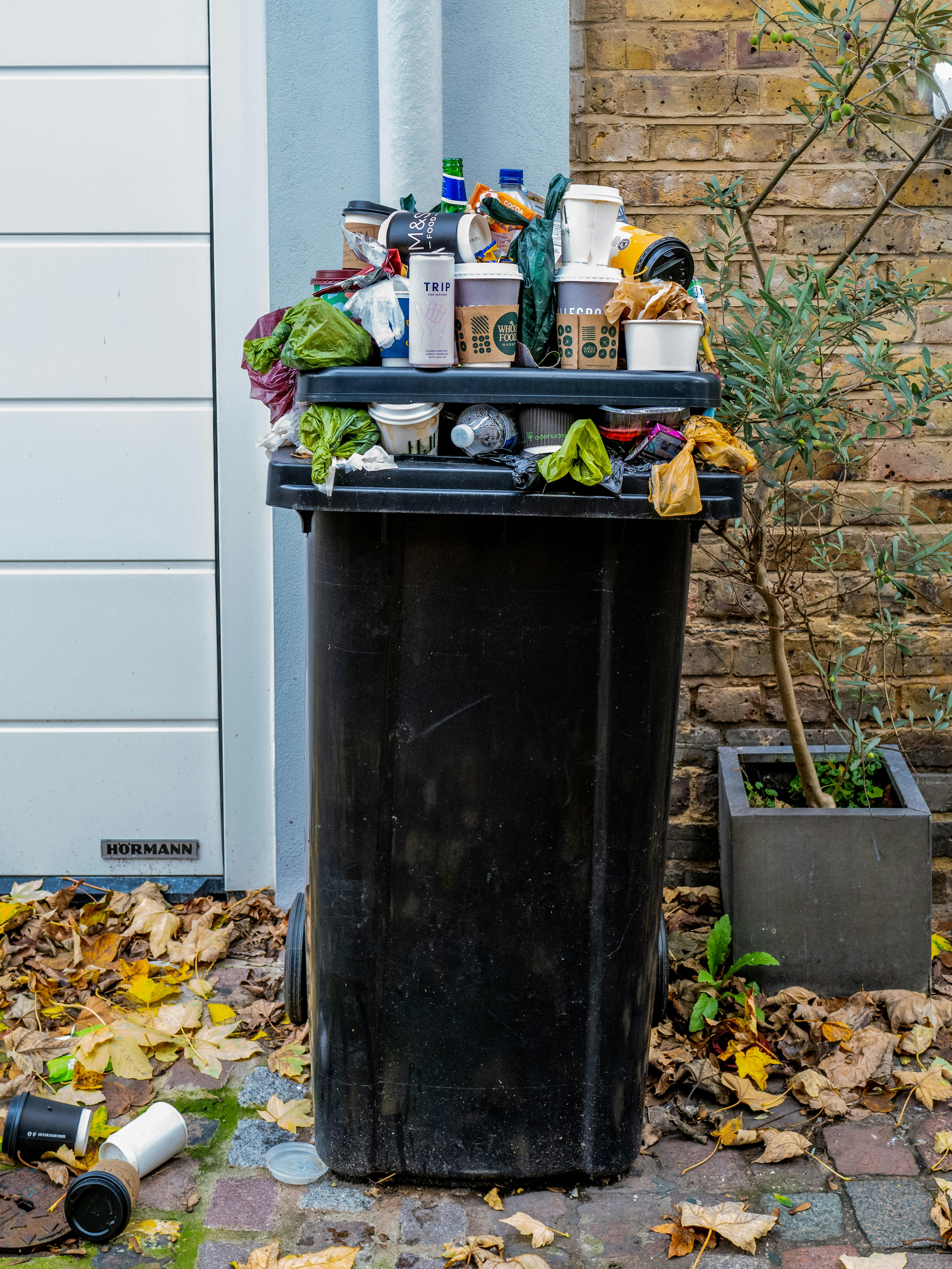 A Black trash can overlowing with trash.