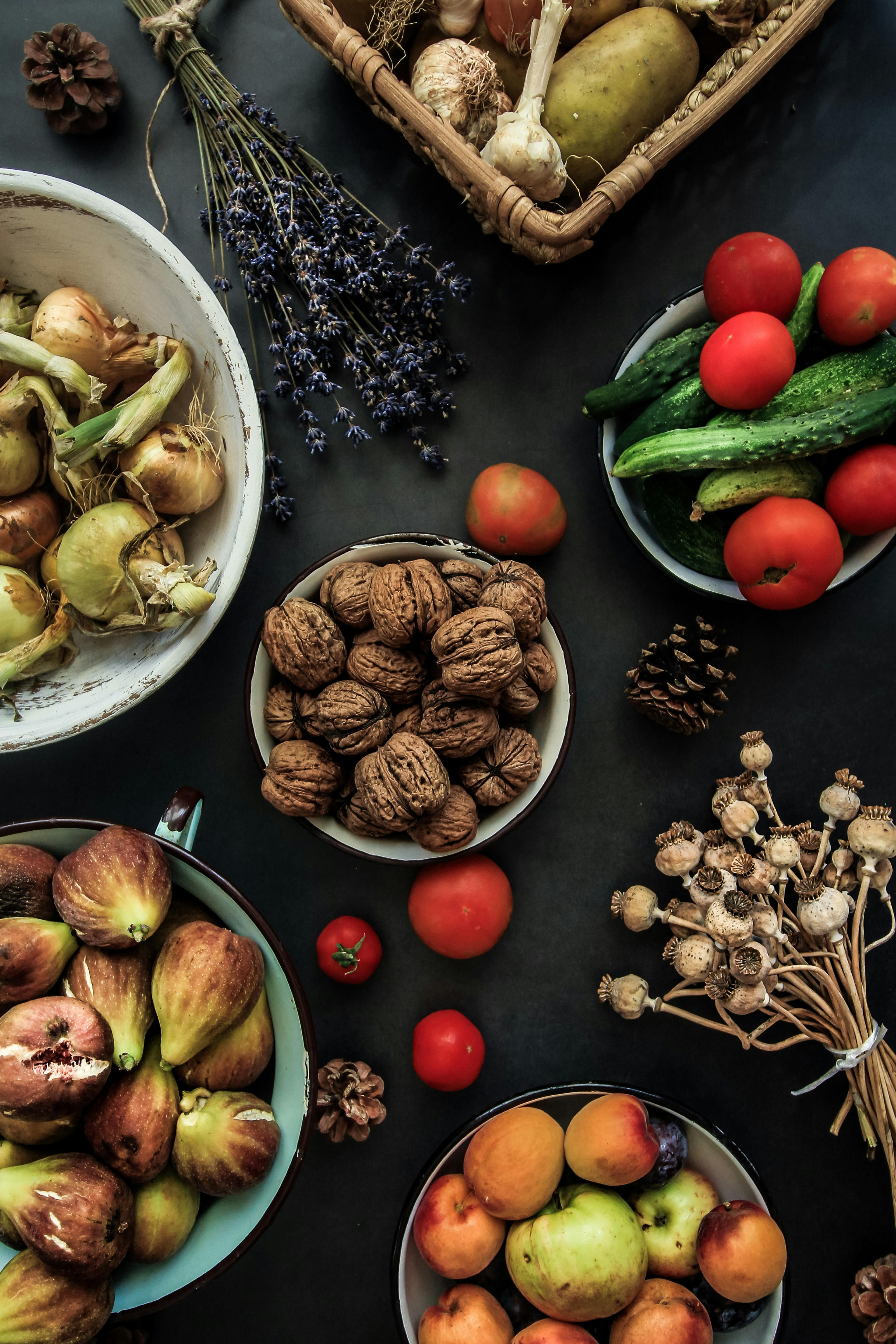 A table with six plates all holding a variety of produce and a single bunch of flowers is on the table.